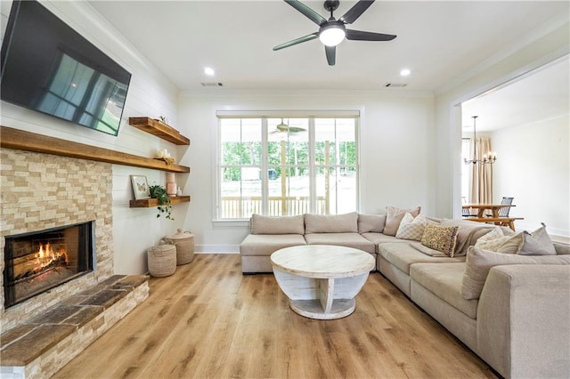 living room featuring a fireplace, ornamental molding, ceiling fan with notable chandelier, and light wood-type flooring