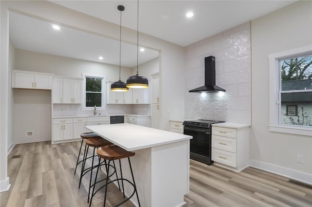 kitchen with tasteful backsplash, wall chimney range hood, white cabinets, black appliances, and a sink