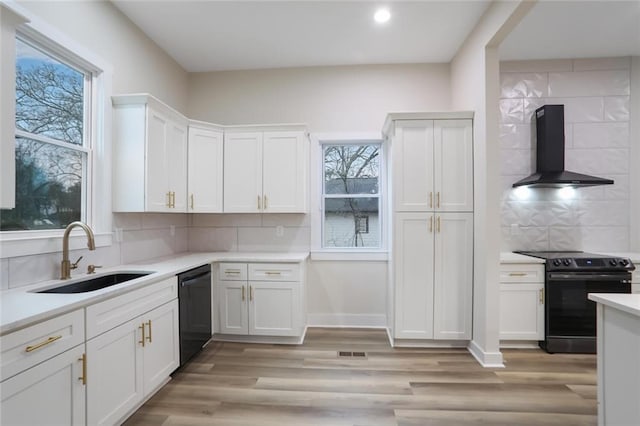 kitchen with black appliances, wall chimney range hood, light wood-style floors, white cabinetry, and a sink