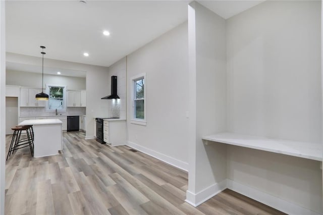 kitchen featuring wall chimney range hood, a breakfast bar area, light countertops, white cabinets, and black appliances