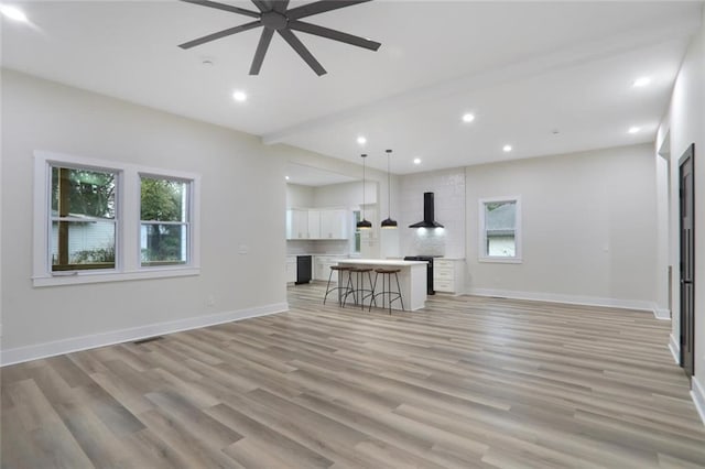 unfurnished living room featuring a ceiling fan, baseboards, light wood finished floors, recessed lighting, and beamed ceiling