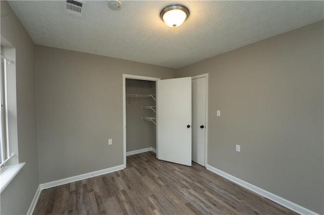 unfurnished bedroom with a textured ceiling, wood finished floors, visible vents, baseboards, and a closet