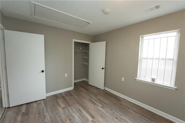 unfurnished bedroom with a closet, visible vents, attic access, wood finished floors, and baseboards