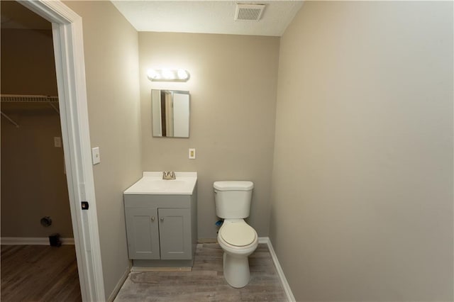 bathroom featuring visible vents, toilet, vanity, wood finished floors, and baseboards