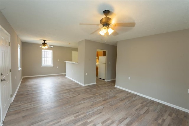 spare room with a ceiling fan, light wood-type flooring, and baseboards