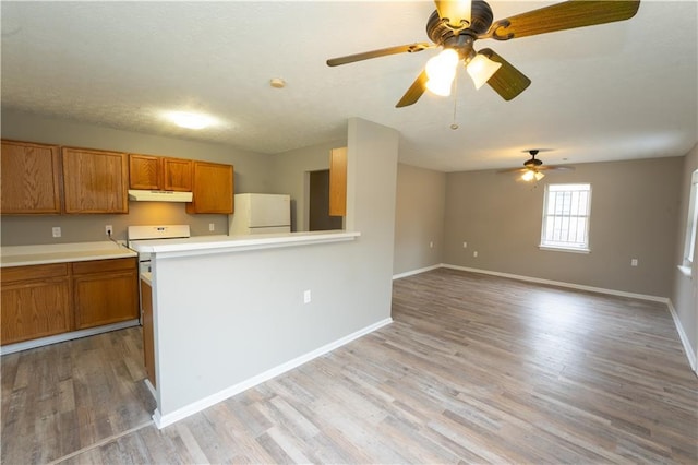 kitchen featuring brown cabinetry, open floor plan, freestanding refrigerator, light countertops, and under cabinet range hood