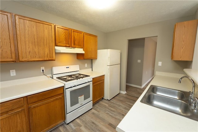 kitchen with white appliances, light countertops, a textured ceiling, under cabinet range hood, and a sink