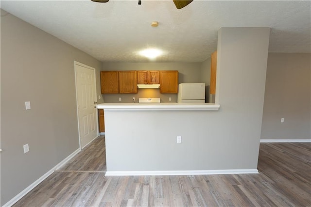 kitchen featuring baseboards, wood finished floors, freestanding refrigerator, light countertops, and under cabinet range hood