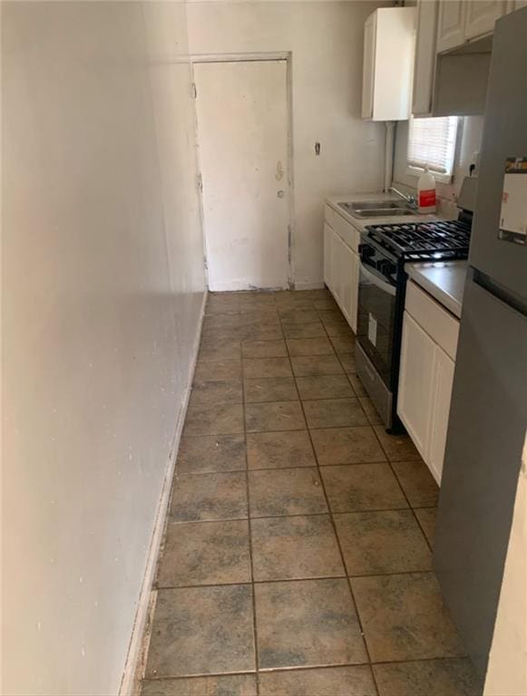 kitchen with appliances with stainless steel finishes, tile patterned flooring, sink, and white cabinets