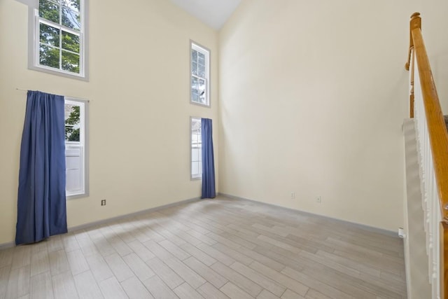 interior space with baseboards, light wood-style flooring, and high vaulted ceiling
