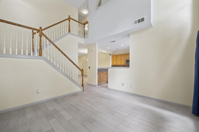unfurnished living room featuring visible vents, stairway, baseboards, a high ceiling, and light wood-style flooring