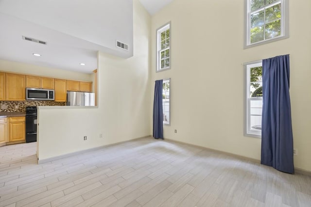unfurnished living room featuring light wood-style floors, a towering ceiling, and visible vents