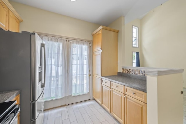 kitchen with dark countertops, light brown cabinets, stainless steel appliances, and a peninsula