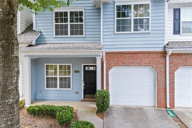 doorway to property with roof with shingles, an attached garage, driveway, and brick siding