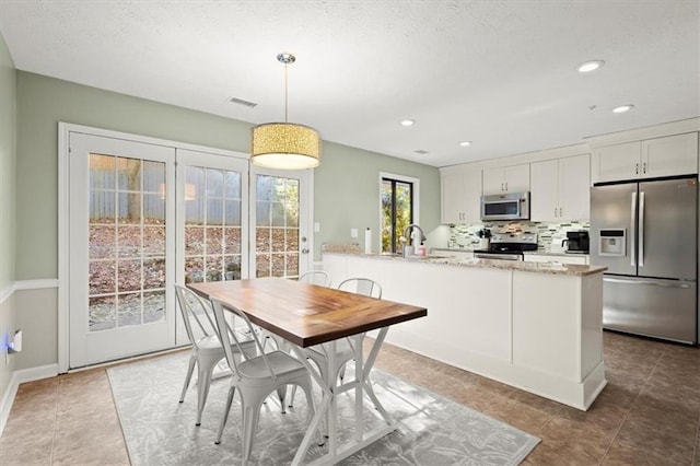 kitchen featuring light stone counters, decorative light fixtures, decorative backsplash, white cabinetry, and appliances with stainless steel finishes