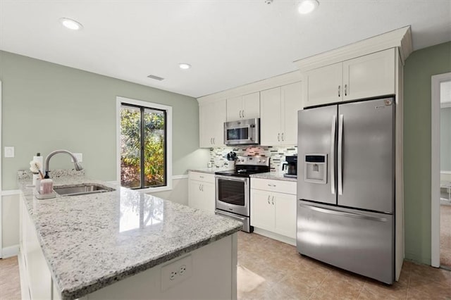 kitchen with light stone counters, stainless steel appliances, backsplash, white cabinetry, and sink