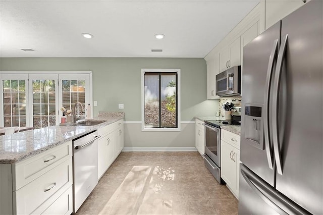 kitchen with sink, white cabinetry, light stone counters, and appliances with stainless steel finishes