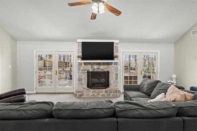 carpeted living room with french doors, ceiling fan, vaulted ceiling, and a stone fireplace