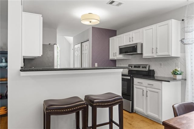 kitchen featuring a breakfast bar area, light wood-style flooring, visible vents, white cabinetry, and stainless steel appliances