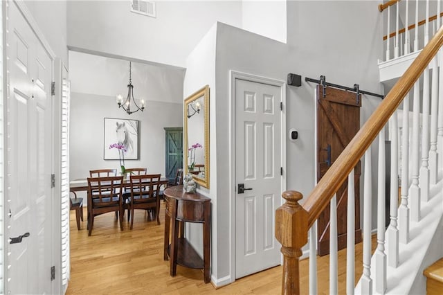 staircase with wood finished floors, a high ceiling, a notable chandelier, visible vents, and a barn door