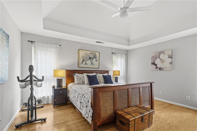 bedroom featuring a tray ceiling, visible vents, light wood-style flooring, and baseboards