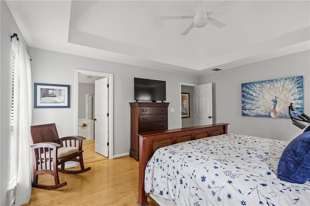 bedroom featuring a tray ceiling, light wood-style flooring, baseboards, ensuite bathroom, and visible vents