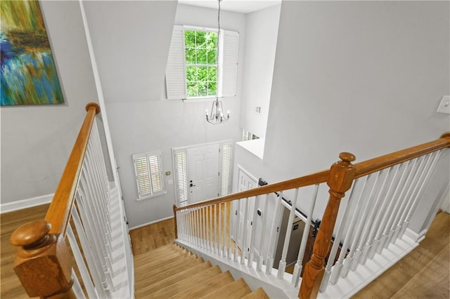 staircase featuring baseboards, an inviting chandelier, a high ceiling, and wood finished floors