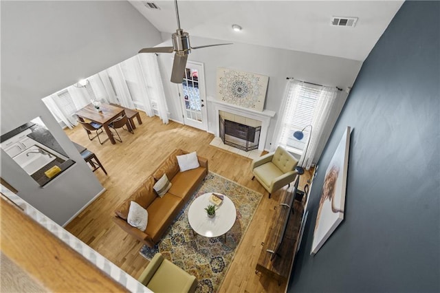 living area with wood finished floors, visible vents, vaulted ceiling, a fireplace, and a ceiling fan