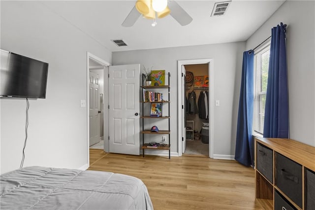 bedroom featuring baseboards, light wood-style flooring, visible vents, and a walk in closet