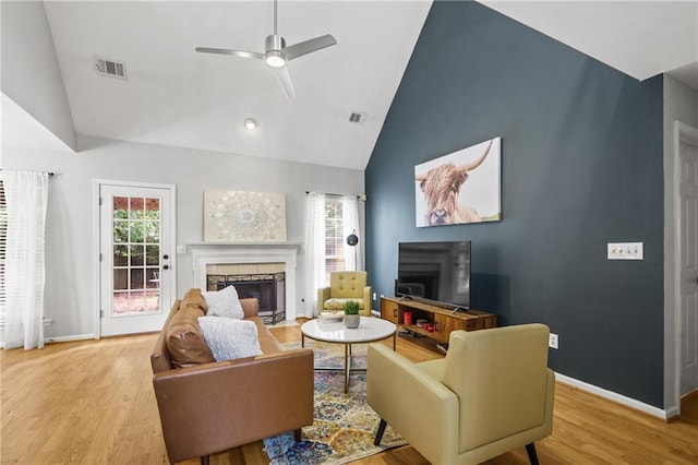 living area with ceiling fan, wood finished floors, a tiled fireplace, and visible vents