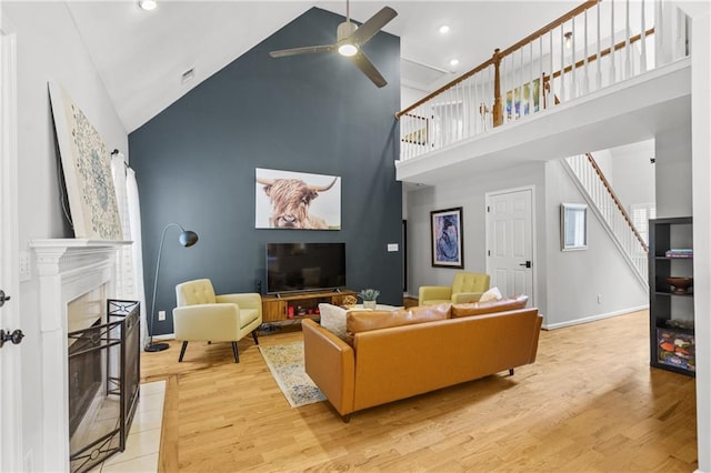 living area featuring stairway, light wood-style flooring, high vaulted ceiling, and a ceiling fan