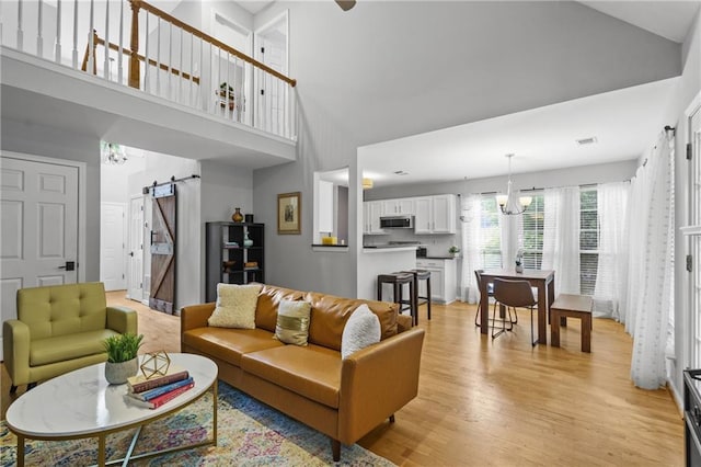 living area featuring a barn door, visible vents, a chandelier, high vaulted ceiling, and light wood-type flooring