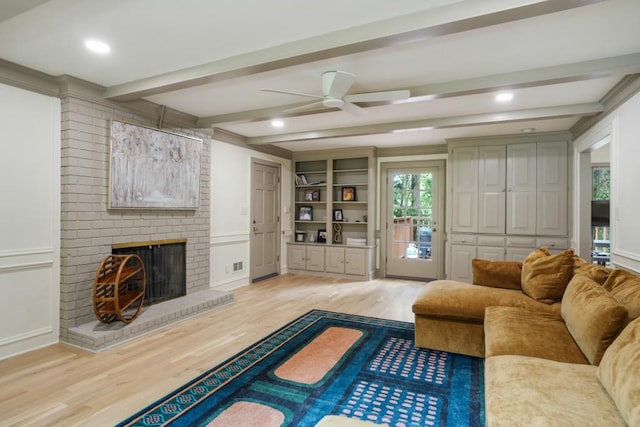 living area featuring built in features, beam ceiling, light wood-style flooring, a fireplace, and a ceiling fan