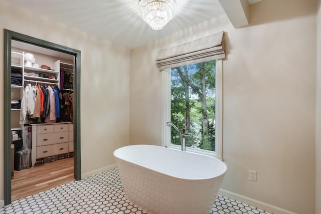 full bathroom featuring a spacious closet, a chandelier, baseboards, and a freestanding tub