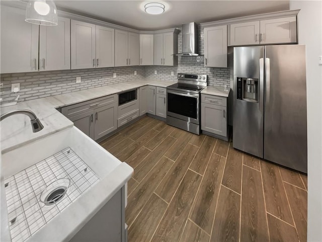 kitchen featuring decorative backsplash, wall chimney exhaust hood, appliances with stainless steel finishes, dark wood-type flooring, and gray cabinetry