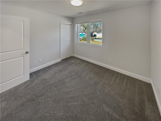 unfurnished bedroom with baseboards, dark carpet, and a closet