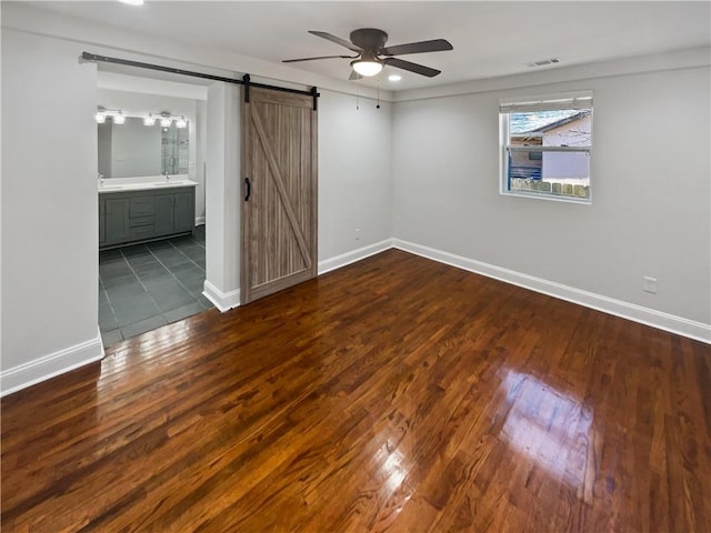 unfurnished bedroom with a barn door, visible vents, baseboards, and wood finished floors