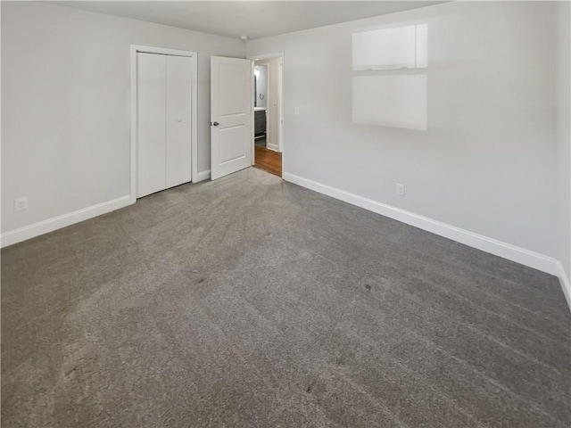 unfurnished bedroom featuring a closet, dark carpet, and baseboards