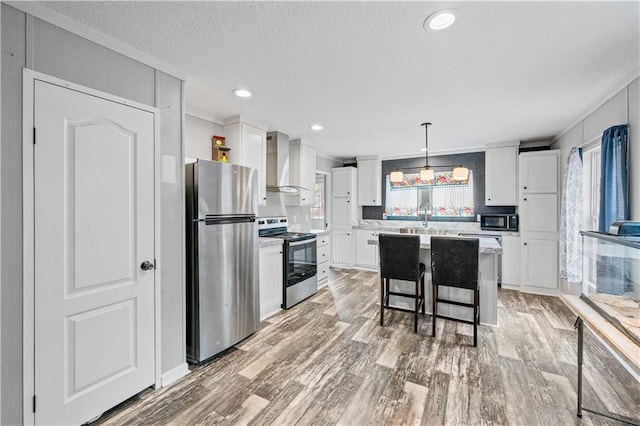 kitchen featuring a kitchen island, appliances with stainless steel finishes, decorative light fixtures, a breakfast bar, and wall chimney exhaust hood