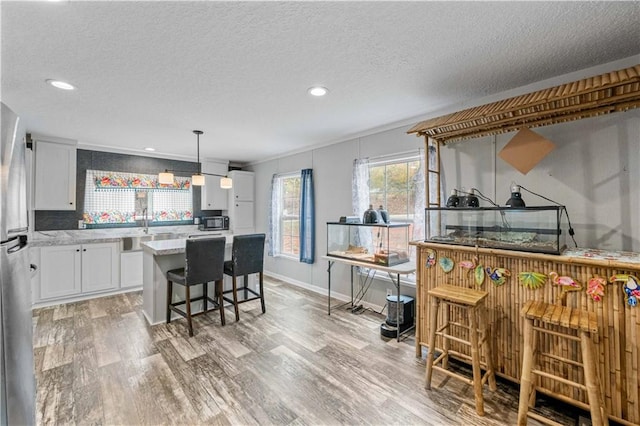 kitchen with light wood-type flooring, pendant lighting, a kitchen breakfast bar, white cabinets, and a center island