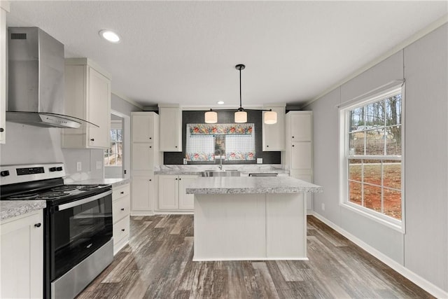 kitchen with wall chimney exhaust hood, sink, hanging light fixtures, electric range, and white cabinets