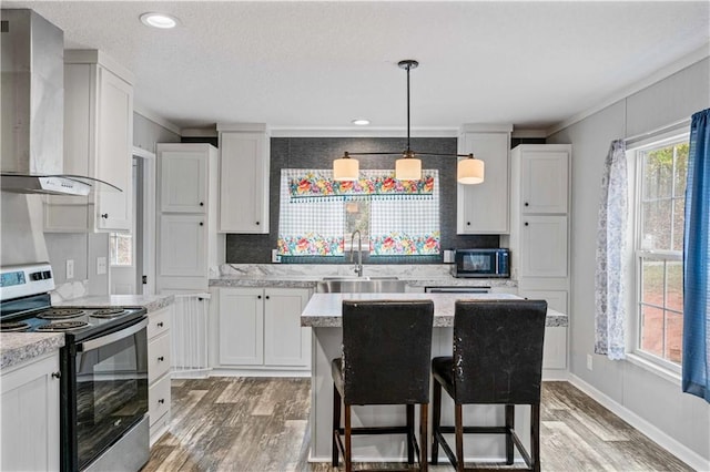 kitchen featuring sink, a breakfast bar area, electric range, wall chimney range hood, and white cabinets