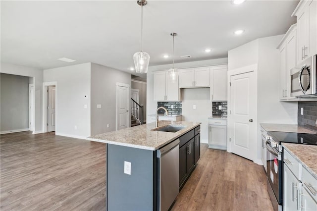 kitchen featuring a center island with sink, appliances with stainless steel finishes, light wood-type flooring, white cabinetry, and a sink