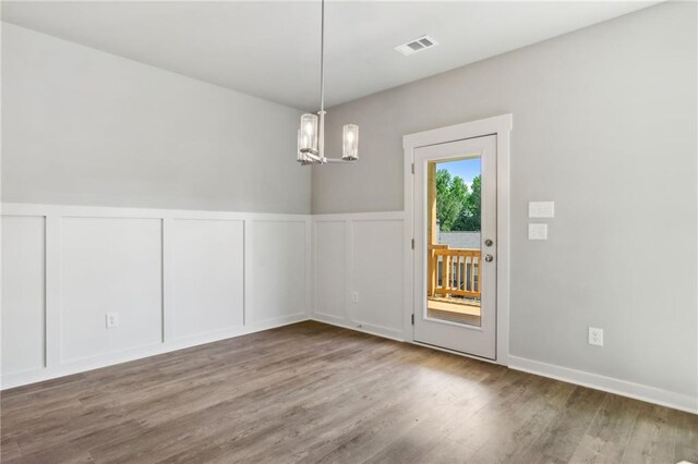 unfurnished dining area featuring a chandelier, a decorative wall, a wainscoted wall, wood finished floors, and visible vents