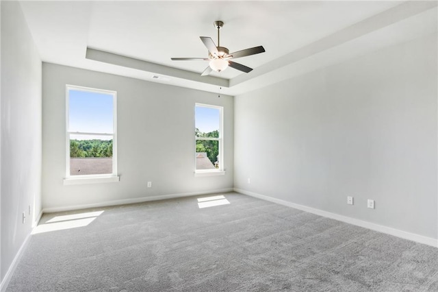 carpeted empty room featuring plenty of natural light, baseboards, a raised ceiling, and a ceiling fan