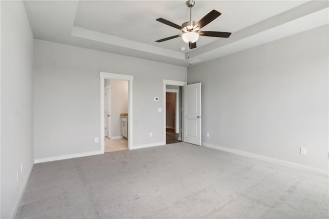 unfurnished bedroom featuring ceiling fan, connected bathroom, light carpet, baseboards, and a tray ceiling