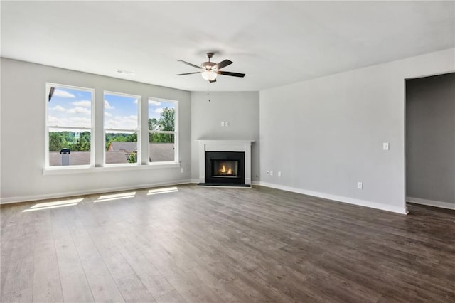 unfurnished living room with a ceiling fan, dark wood-style flooring, a lit fireplace, and baseboards