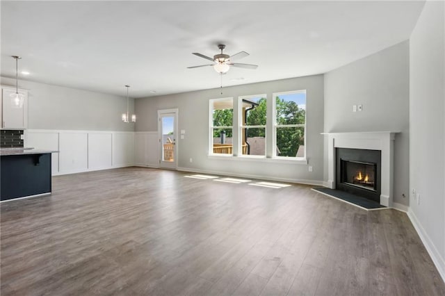 unfurnished living room with a warm lit fireplace, ceiling fan, dark wood-style flooring, and baseboards