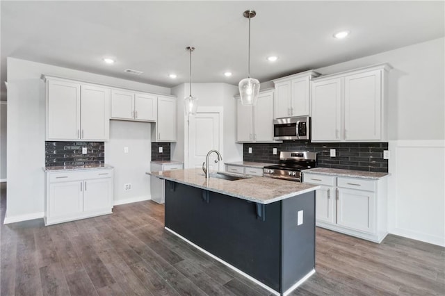 kitchen featuring stainless steel appliances, dark wood-type flooring, white cabinets, a sink, and an island with sink