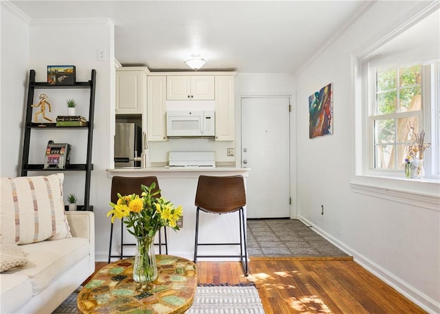 kitchen featuring white microwave, a kitchen breakfast bar, dark wood-style flooring, freestanding refrigerator, and crown molding